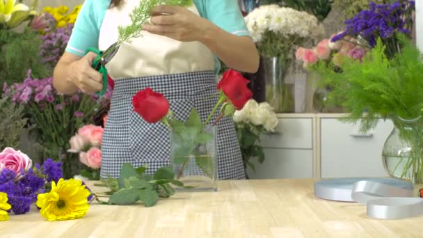 Dolly shot van bloemist vrouw snijden en regelen van bloemen in een glazen vaas — Stockvideo
