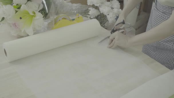 Цветочница готовит бумагу к обертыванию цветочным букетом, неоцененным тоном — стоковое видео