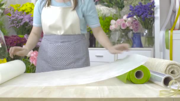 Dolly Shot von Blumenhändlerin beim Vorbereiten von Papier zum Einwickeln eines Blumenstraußes — Stockvideo