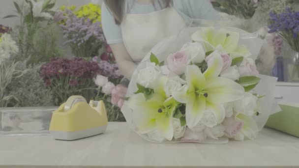 Dolly tiro de florista mujer envolviendo un ramo de flores con papel, tono sin graduar — Vídeo de stock