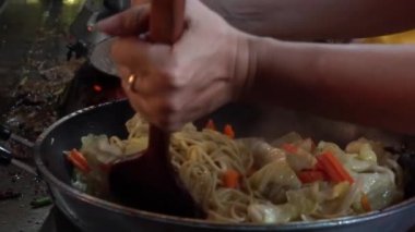 Yellow noodles are being fried in hot frying pan in slow-motion