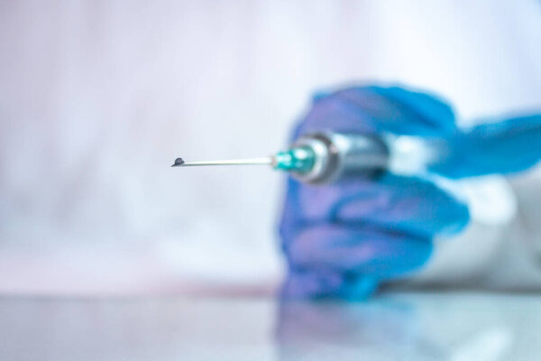 drop of vaccine in syringe for the treatment of covid 19 with the use of blue gloves