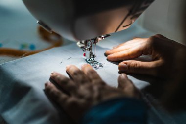 Gri kumaş ve iğneli dikiş makinesi kullanan bir kadın.