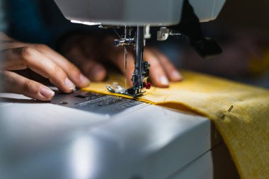 Sarı kumaş ve iğneli dikiş makinesi kullanan bir kadın.