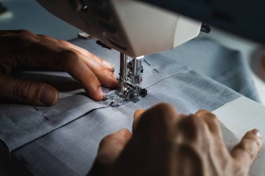 Gri kumaş ve iğneli dikiş makinesi kullanan bir kadın.