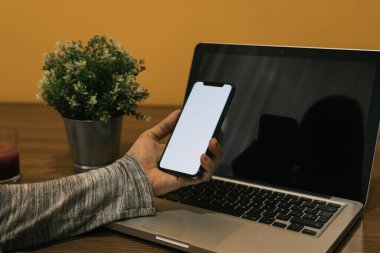 Ahşap bir masada dizüstü bilgisayar ve telefonla çalışan hamile bir beyaz kadın.