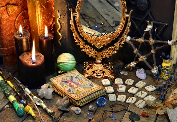 Tarot cards, magic wands, runes, black candles with mirror and old books. Occult, esoteric, divination and wicca concept. Mystic and vintage background