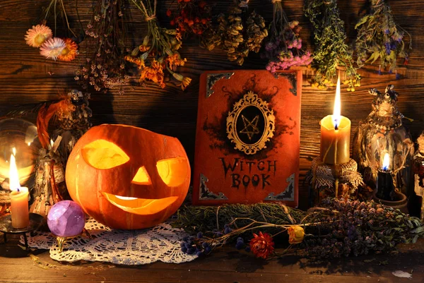 Halloween still life with witch book, Jack O Lantern pumpkin, candles and herbs on witch table.