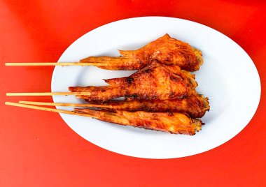 Kolay taşınması için ızgara tavuk kanadı, Tayland 'da bir sokak restoranında mavi bir tabağa konur.