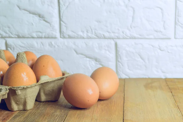 Chicken eggs in a paper tray and eggs placed on a wooden table in the kitchen with a bricked background