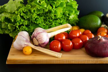 Ahşap kesim tahtasındaki malzemeler taze sarı ve kırmızı kiraz domateslerinden salata, marul, avokado, sarımsak ve soğan, yakın plan..