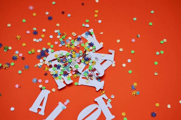 carved letters of the day of the fool mixed with multicolored confitti on an orange background