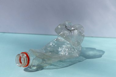 Buruşmuş plastik şişe, şişedeki güneşli gölgenin mavi ve beyaz arka planına dayanır.