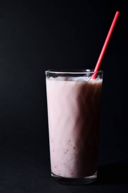 Kırmızı kağıt tüplü, cam bardakta çilek şuruplu milkshake.