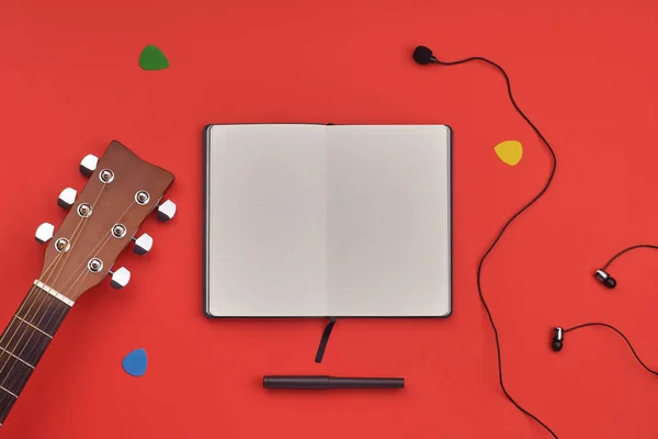 Guitar learning concept. Notebook with a place for text, guitar, headphones and microphone on red background. Minimal flat lay view