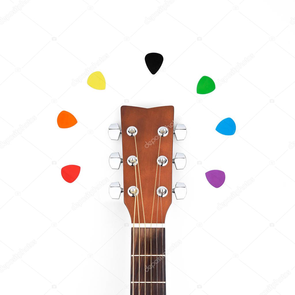 Colorful picks around acoustic guitars headstock. Isolated flat lay
