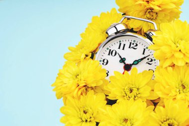 Sarı çiçeklerle çevrili çalar saat.