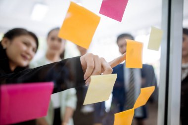 İş adamları ofiste toplanıyor ve iş arkadaşlarına ofis beyin fırtınası stratejisi atölyesinde yapışkan notlar üzerinden açıklama yapıyorlar.