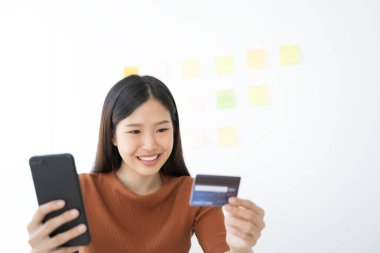 Genç Asyalı kadın akıllı telefon ve kredi kartı kullanıyor. İnternetten alışveriş.