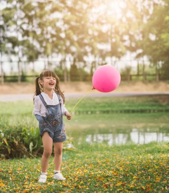 Parkta balonla gezen mutlu küçük kız portresi.