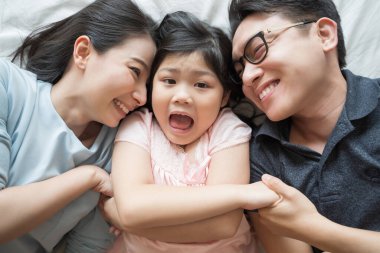 Mutlu Asyalı bir ailenin portresi. Yatakta uzanmış, yukarı bakıyor ve el ele tutuşuyor.