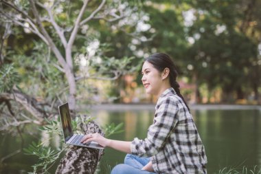Açık hava parkında dizüstü bilgisayar kullanan mutlu Asyalı kadın..