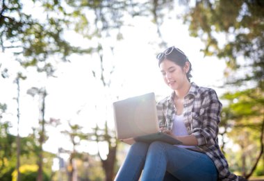 Açık hava parkında dizüstü bilgisayar kullanan mutlu Asyalı kadın..