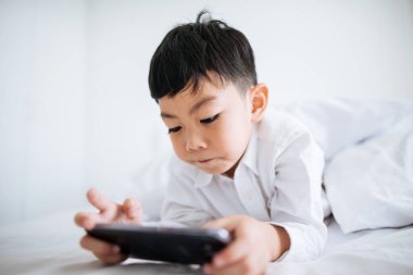 Tablet kullanan çocuk, yatakta yatıyor.