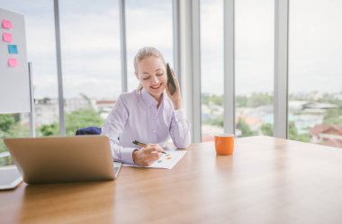 Ofiste dizüstü bilgisayarda çalışan bir kadın telefonda konuşurken, iş kadını portresi 