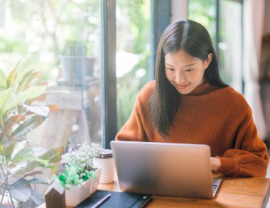 Bilgisayarla çalışan mutlu genç Asyalı kadın ekrana bakıyor.