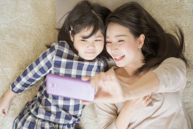 Anne, küçük kızıyla özçekim yapıyor. Akıllı telefon kamerasıyla kızı Asian aile kavramını kullanıyor.