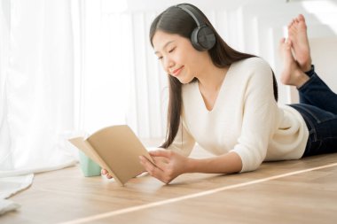 Asyalı kadın kitap okuyor ve evde kahveyle rahatlıyor..