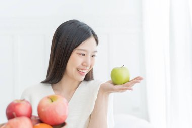 Yeşil elma ve kırmızı elma gösteren genç bir Asyalı kadın.