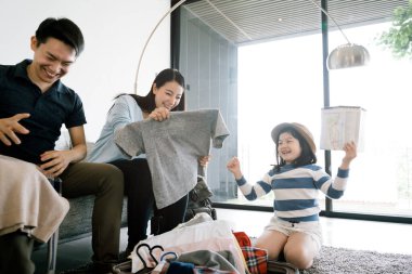Mutlu Asyalı aile eve gitmek için hazırlanıyor. Anne kız ve baba yolculuk için bavullarını hazırlıyorlar..