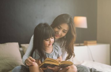 Anne ve kızı evde kitap okuyorlar.