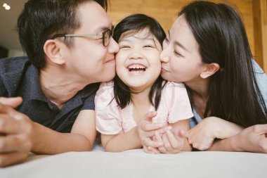 Asyalı ebeveynler küçük kızlarını yanaklarından öpüyor. aile portresi.