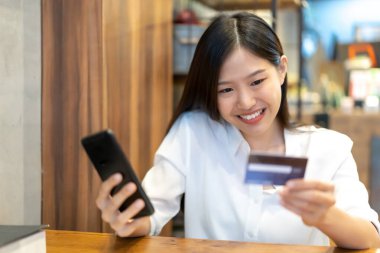 Genç Asyalı kadın akıllı telefon ve kredi kartı kullanıyor. İnternetten alışveriş.