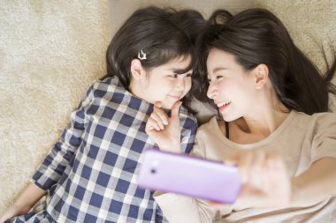 Anne, kızı Asian aile kavramı ile göz teması kurarken küçük kızıyla akıllı bir telefon kamerası kullanıyor.