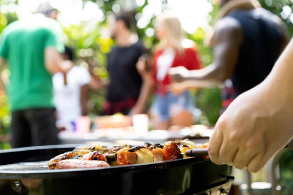 hand of bbq grilling and friends having barbecue party, outdoors