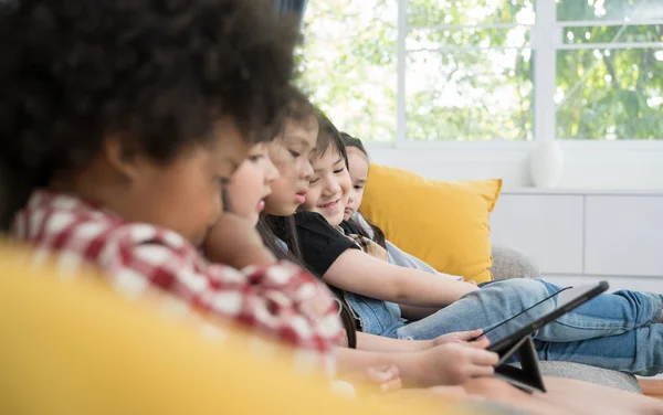 group of little children watching film movie cartoon together on digital tablet. Kids playing with tablet with friends at home