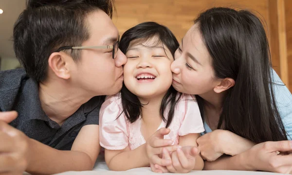 Asyalı ebeveynler küçük kızlarını yanaklarından öpüyor. aile portresi.