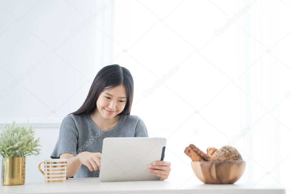 Young Asian woman using tablet at home and having breakfast in the morning .She reading on tablet.