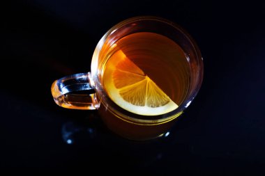 Bir cam kupa bir güzel çay ve limon ile siyah cam üzerinde duruyor. Yakın çekim