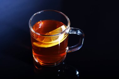Bir cam bardak limonlu çay siyah cam üzerinde duruyor. Bir fincan çay güzel cam yansıtılır