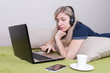 Bir kadın dizüstü arıyorum yeşil bir kanepe yastık karnına yatıyor. Yakındaki telefon ve bir fincan kahve