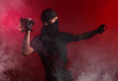 Protestocu bir adam kırmızı arka plana yanan bir şişe fırlatıyor. Duman girdapları