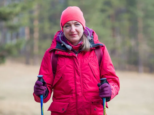 Girl in a red jacket with walking sticks for Finnish walking in nature. Autumn day, hiking