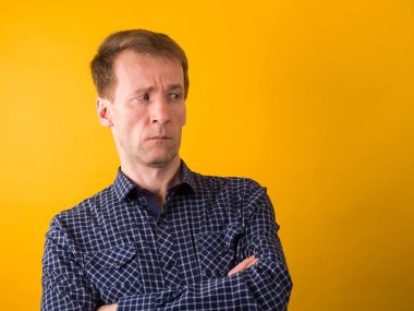 The disgruntled guy in the dark blue shirt frowns. Studio photography on a yellow background