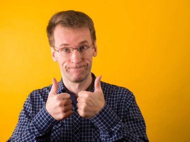 Cheerful guy in a dark blue shirt smiles and shows thumbs up. Studio photography on a yellow background