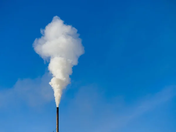 White smoke comes out of a black chimney in the blue sky. Ecology theme